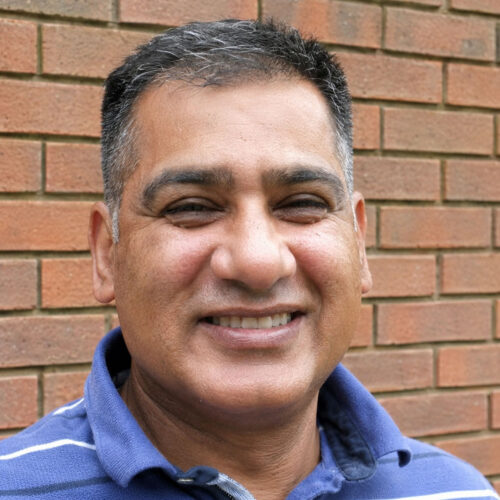Baiju smiling in front of a red brick wall